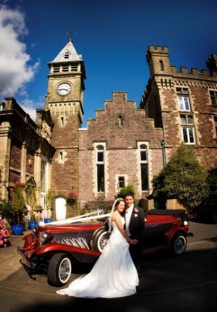 Wedding Venue in Wales, bride and groom by red car Craig y Nos Castle courtyard clocktower