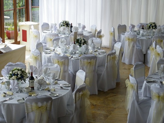 Pale yellow ribbons on white chair covers match in with the yellow floral centrepieces on each wedding table Craig y Nos Castle Wedding Venue Swansea Conservatory Wedding Breakfast pale yellow ribboned chair covers