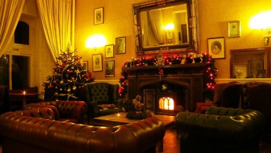 Craig y Nos Castle Patti Bar with roaring log fire, Christmas tree in corner, chesterfield sofas around fire
